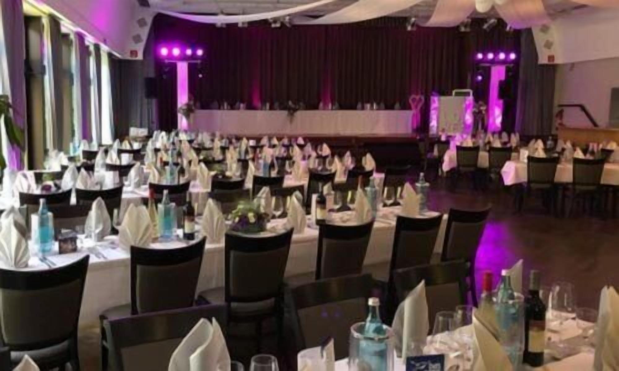 Een feestzaal met rijen tafels gedekt voor een diner, elk met witte tafelkleden en servetten.