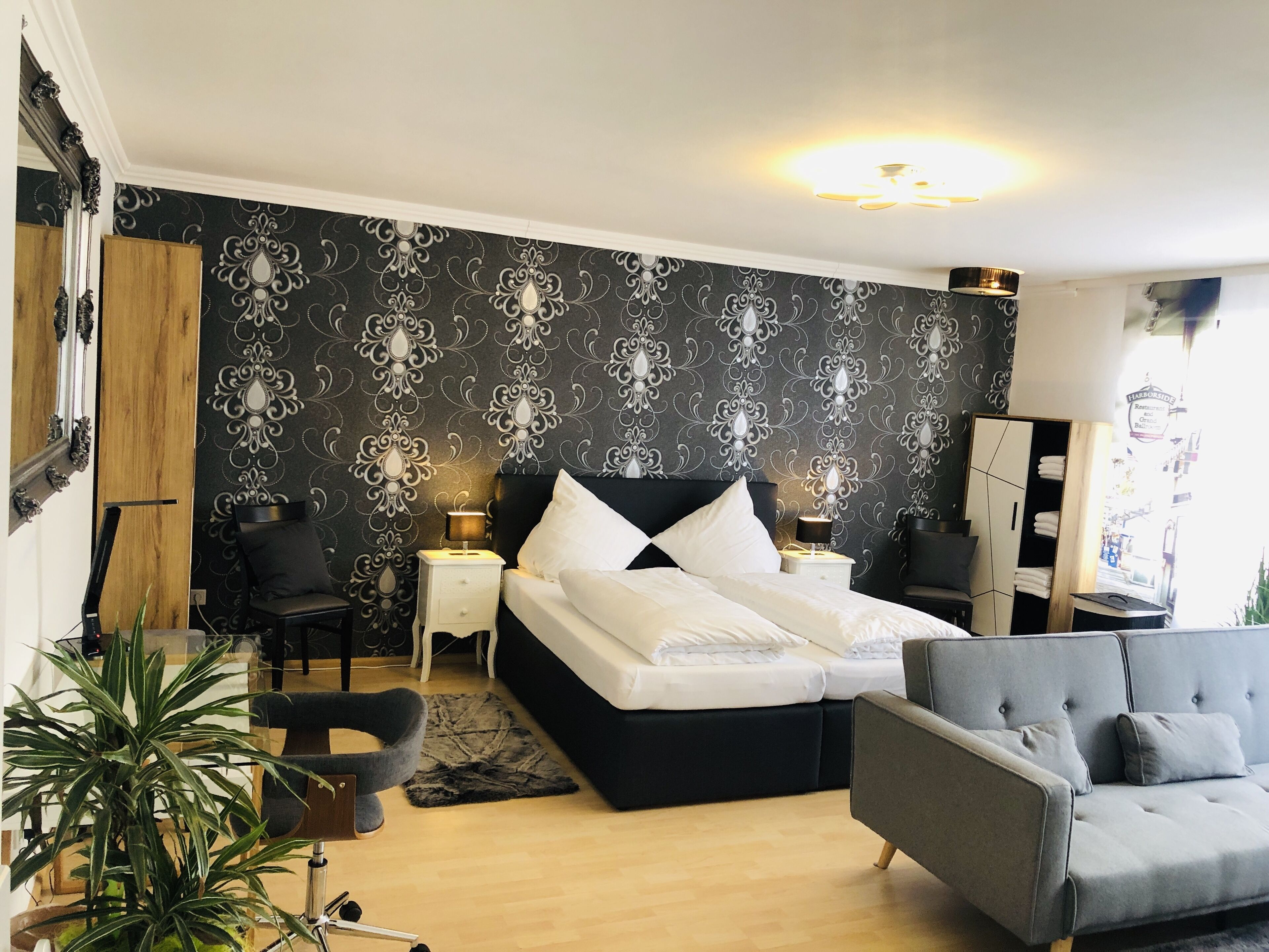 Un dormitorio moderno con papel tapiz a cuadrícula blanco y negro, una cama grande con ropa de cama blanca, un sillón gris y un armario de madera.