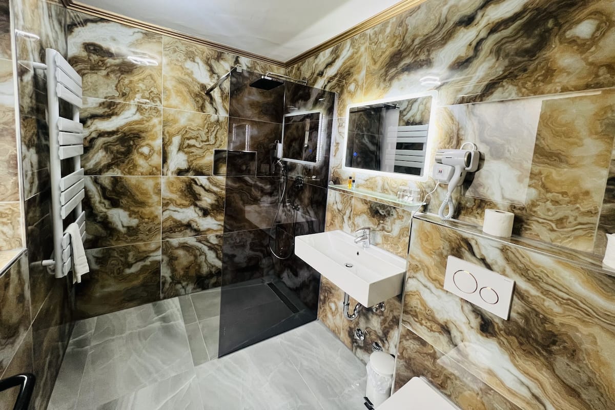 Une salle de bain avec des murs en marbre, une douche en verre, un meuble-lavabo et un miroir.