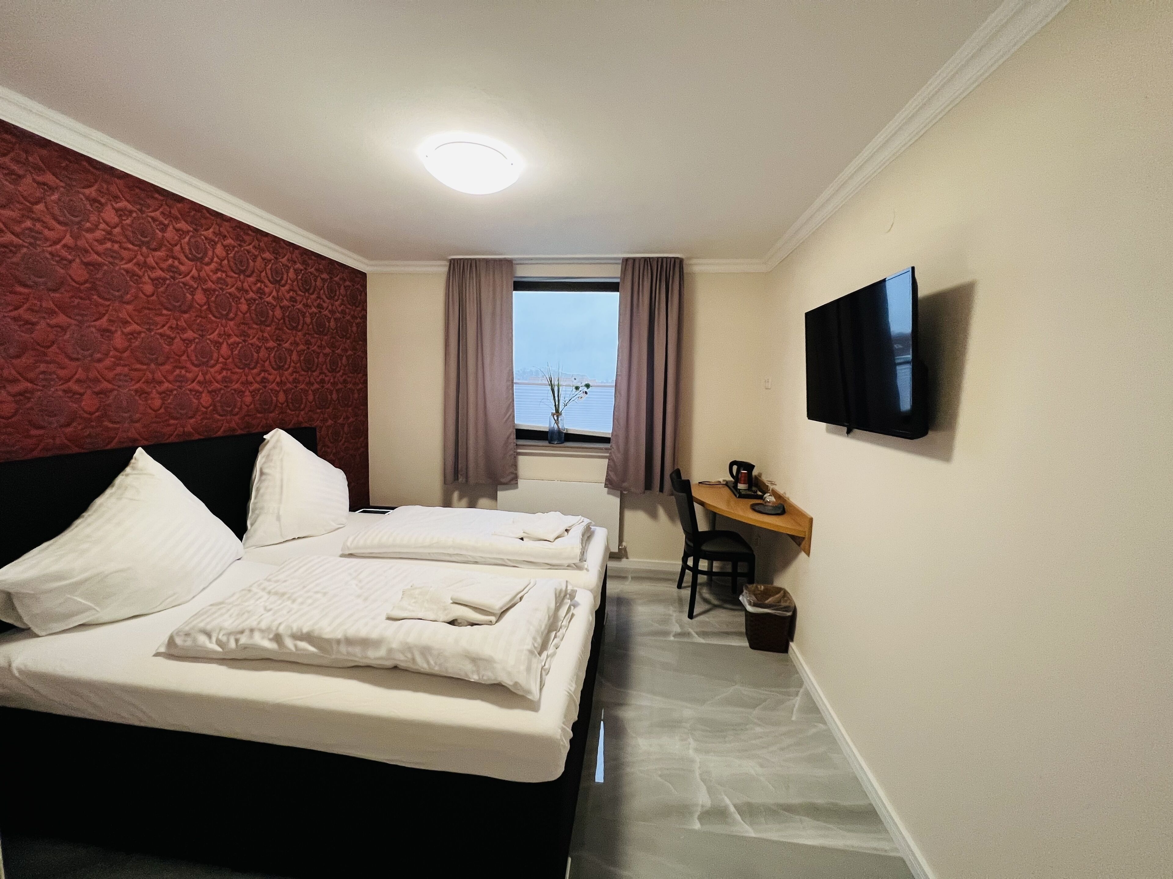 Quarto de hotel com duas camas, uma escrivaninha, uma cadeira, uma televisão e uma janela com vista.