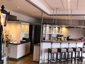 Een moderne keuken met witte kasten, een bar voorzien van krukken, en een hanglamp.