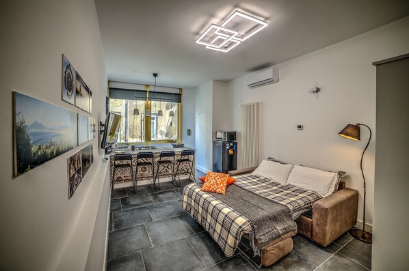 Une chambre d’hôtel de taille réduite, comprenant un lit, un bureau et une kitchenette.