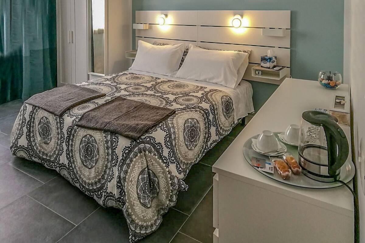 A neatly arranged hotel room with a bed, bedside table, and a small kitchenette area.