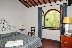 Une chambre à coucher avec un lit, une chaise, une table de chevet, une lampe et une fenêtre avec des rideaux.