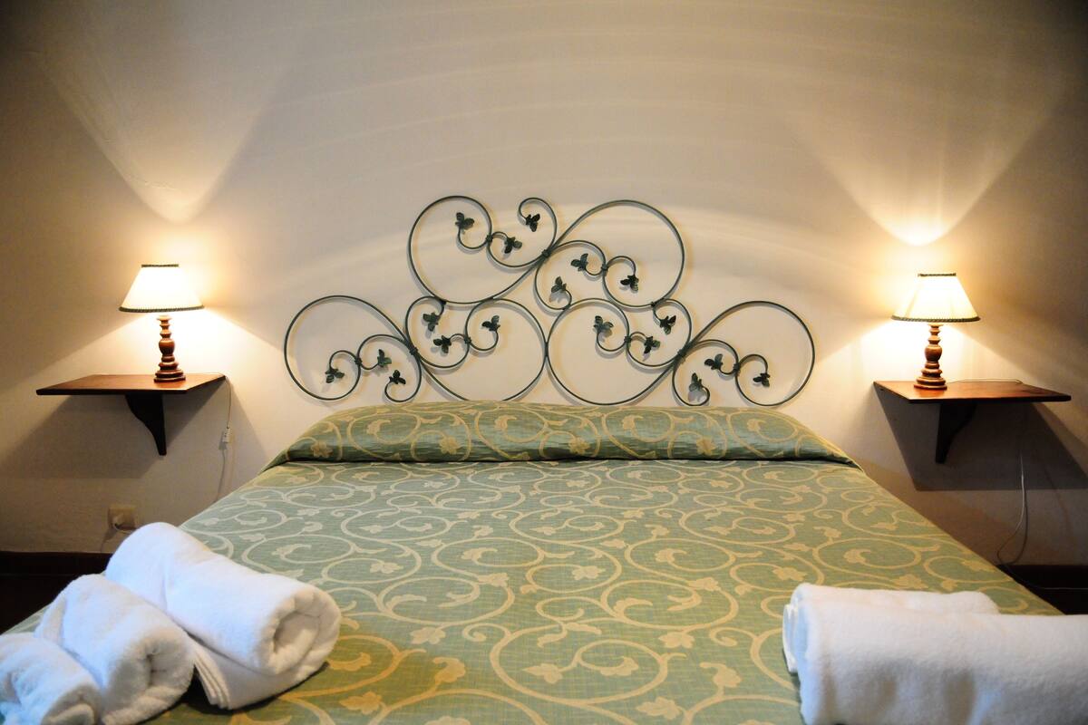 Een opgemaakt bed met een beddengoed met een patroon, twee nachtkastjes met lampen en een decoratieve muurkap.