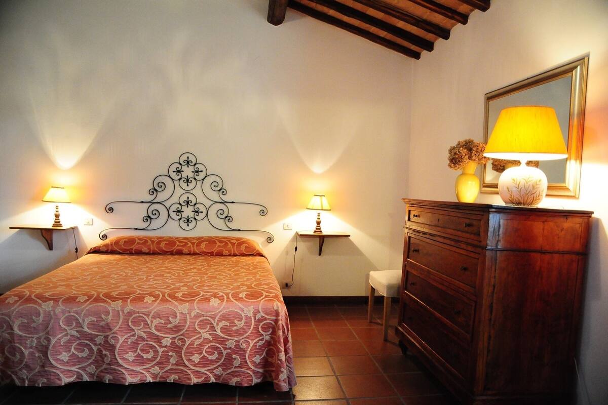 Een slaapkamer met een bed, twee bedlampen, een houten dressoir en een spiegel aan de muur.