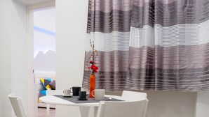 Un coin repas avec une table ronde, des chaises blanches et un vase rempli de fleurs rouges.