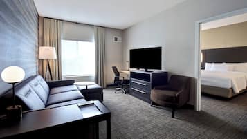 Ein Hotelzimmer mit einer Couch, einem Schreibtisch mit Stuhl, einem Fernseher und einem Bett.
