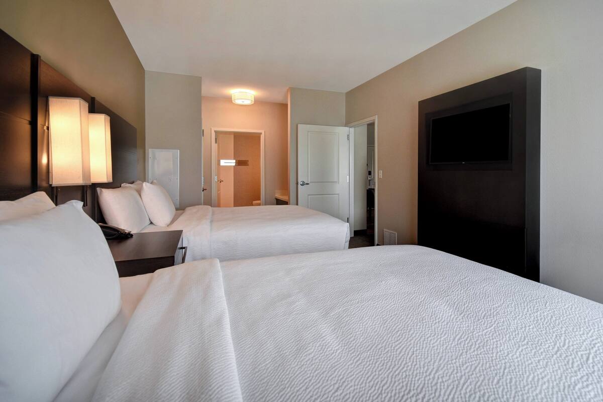 A hotel room with two beds, a TV, a desk, and a lamp.