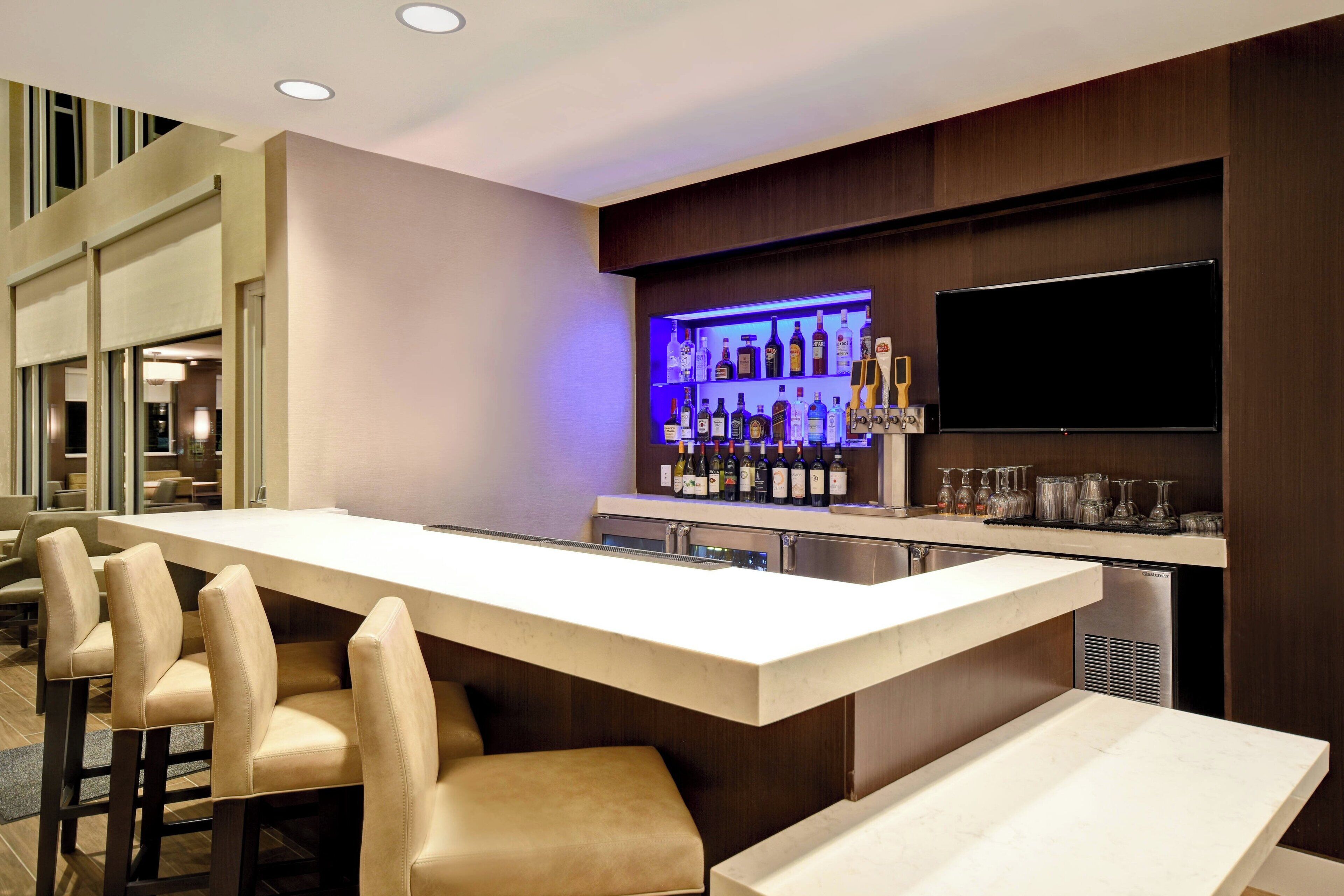 Un espace bar moderne doté d’un long comptoir, de tabourets de bar, d’un meuble à vin et d’un téléviseur à écran plat.