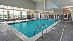 An indoor swimming pool with clear water, surrounded by grey tiled flooring and walls, large windows offering views of the outside, and a lifeguard station with a ladder. - Residence Inn by Marriott Middletown Goshen (Middletown)