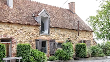 A stone building with a sloped roof, wooden shutters, and a small window with a triangular pediment.