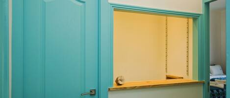A room with a teal door, a small wooden shelf, and a bed with a blue and white patterned bedspread.