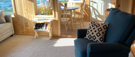 A cozy cabin interior with a wooden interior, a dining area with a table and chairs, and a view of the water through large windows.
