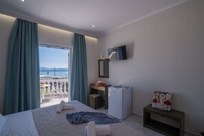A hotel room with a bed, a desk, a small refrigerator, a TV, and a balcony with curtains. - Christina Hotel Petriti (Corfu)