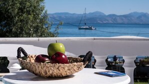 A table with a woven basket containing apples and a book, overlooking a body of water with a sailboat. - Christina Hotel Petriti (Corfu)