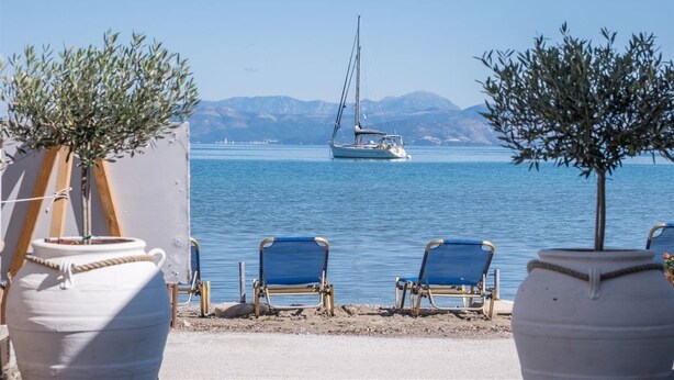 A seaside view with a sailboat, beach chairs, and olive trees. - Christina Hotel Petriti (Corfu)
