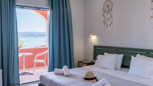 A hotel room with a bed, a nightstand, a dreamcatcher, a straw hat, and a view of the sea through a glass door. - Christina Hotel Petriti (Corfu)