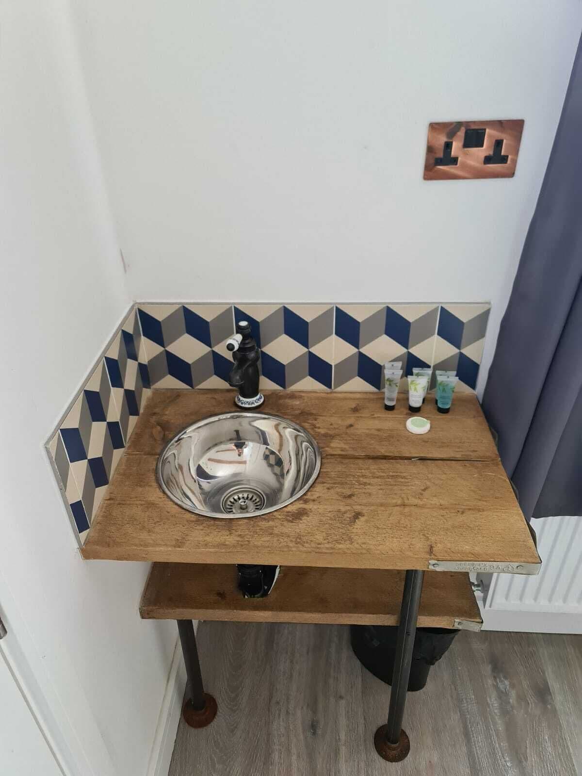 Une salle de bain avec un meuble-lavabo en bois, un évier en acier inoxydable et un revêtement mural en carreaux aux motifs géométriques.