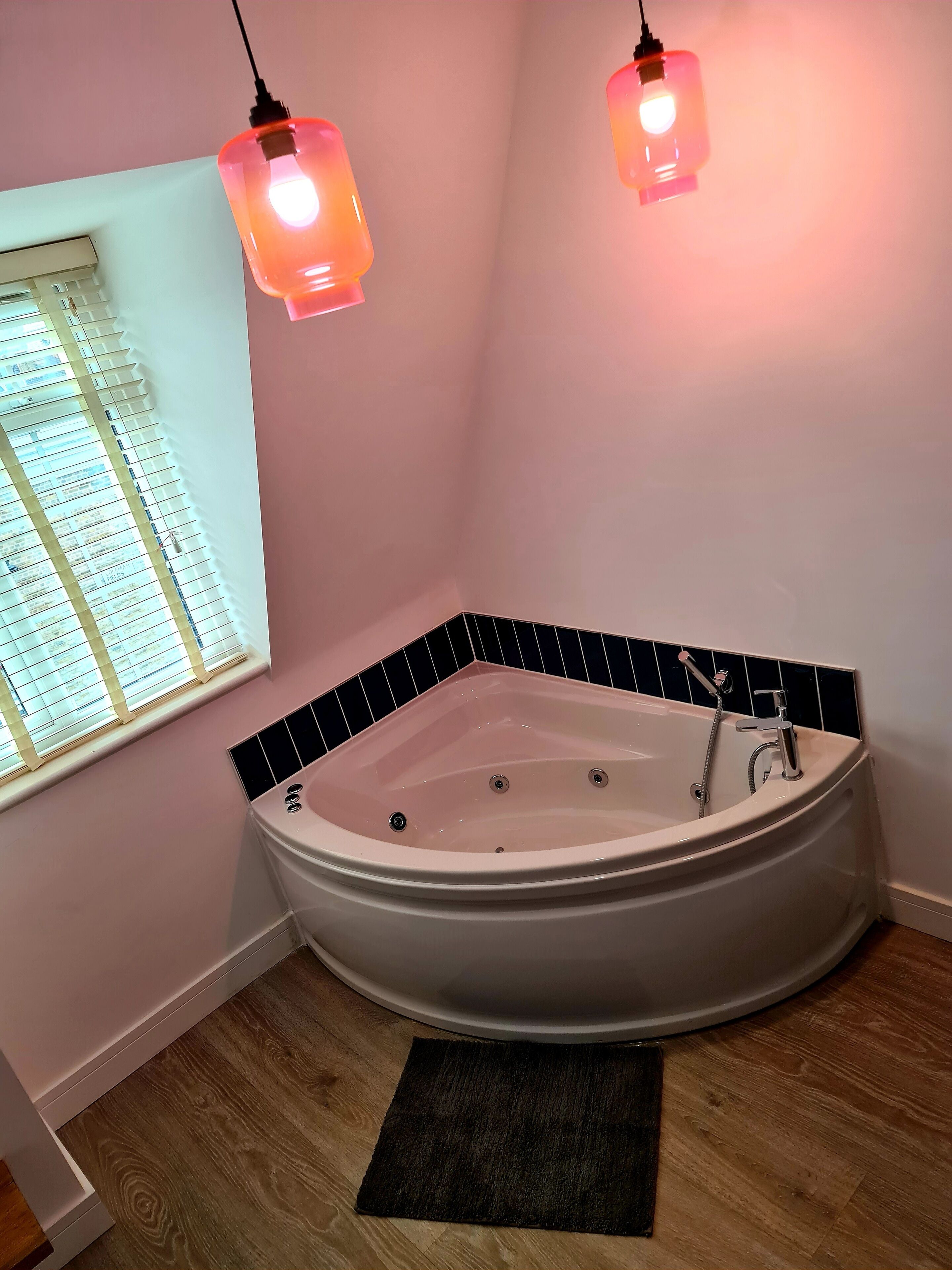 A bathroom with a freestanding bathtub, a window with blinds, and two pendant lights.