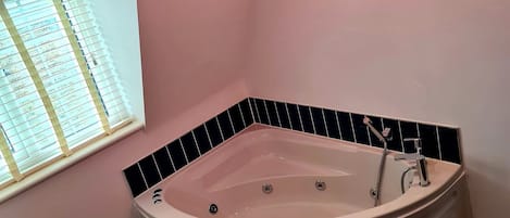 A bathroom with a freestanding bathtub, a window with blinds, and two pendant lights.