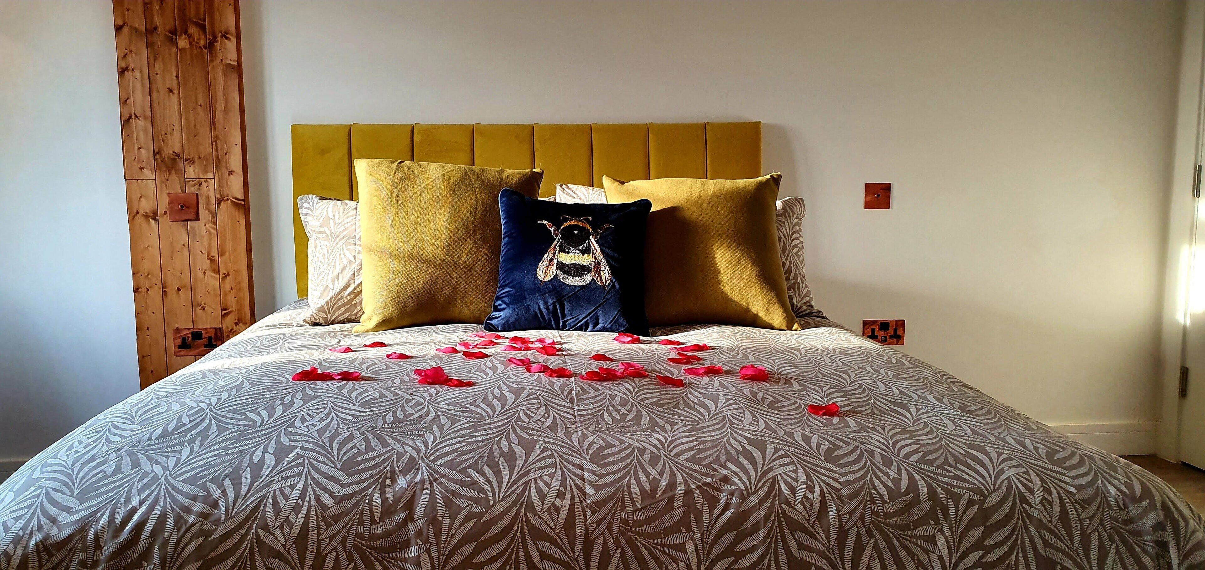 A bed with a patterned bedspread, multiple pillows, and rose petals scattered on the bed.