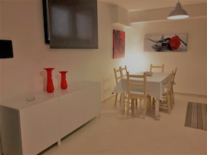 A dining area with a table and chairs, a white cabinet, and two red vases on the cabinet.