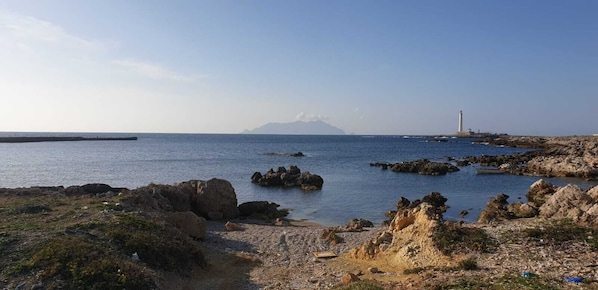 A coastal landscape with rocky terrain, a lighthouse, and a distant mountain.