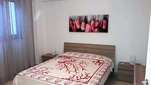 A bedroom with a bed, nightstands, a wall-mounted picture, and a window with curtains.