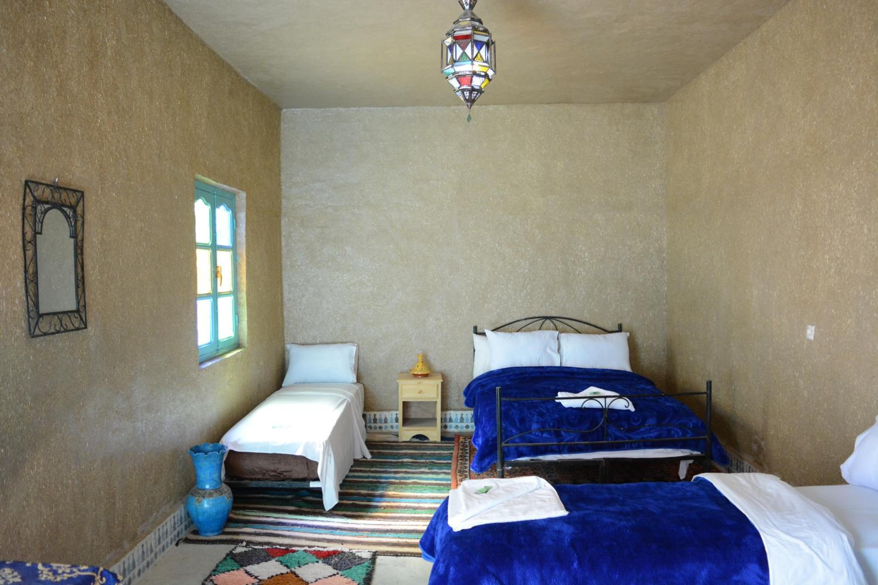 A bedroom with two beds, a window, a hanging lamp, and a small bedside table.