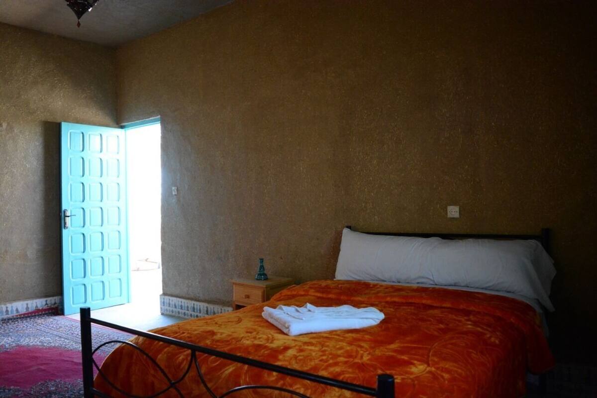 Une chambre à coucher avec un lit, une table de chevet, une porte bleue et une vue sur l’extérieur.