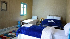 Een kamer met twee bedden, een klein tafeltje, een raam en een decoratief vloerkleed.