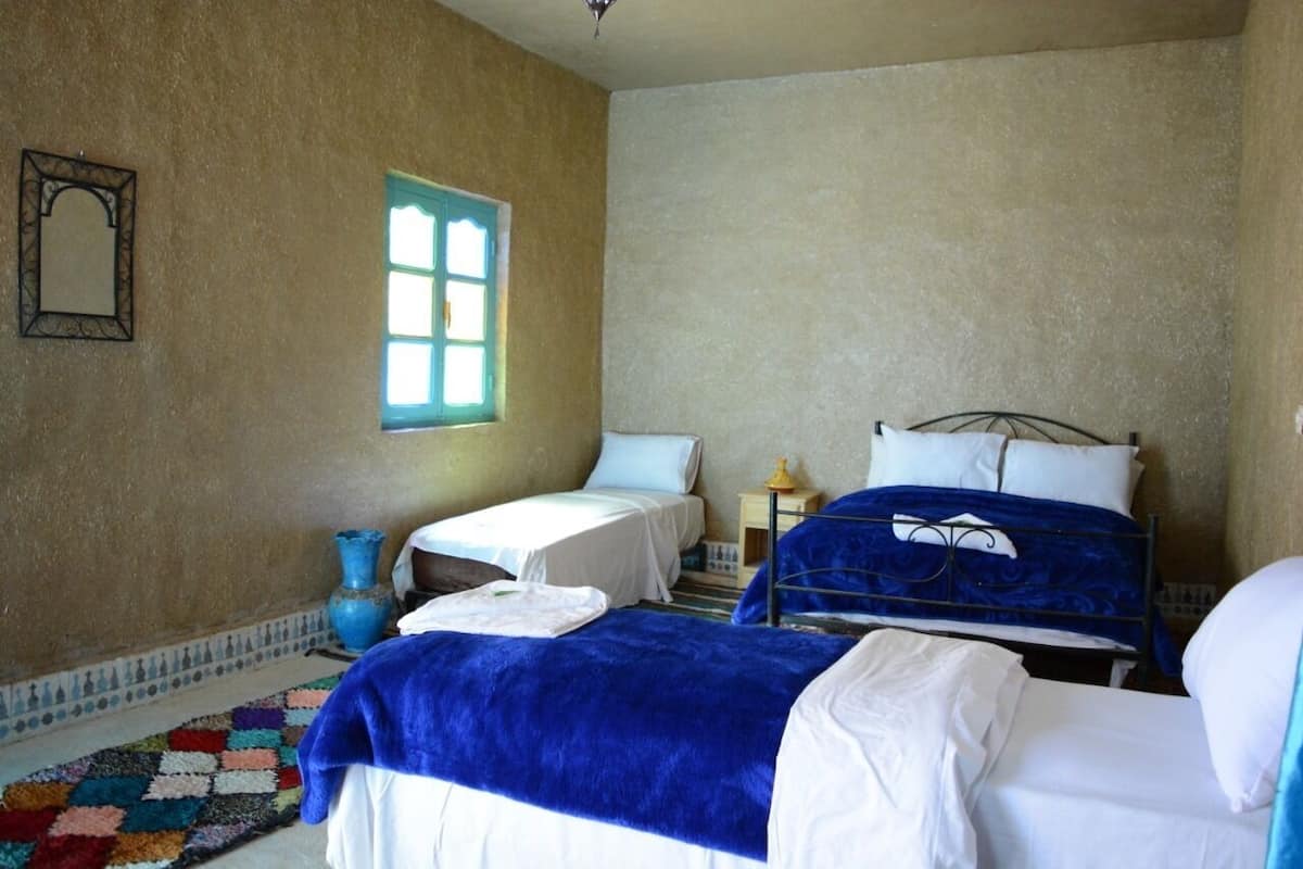 Une chambre avec deux lits, une petite table, une fenêtre et un tapis décoratif.