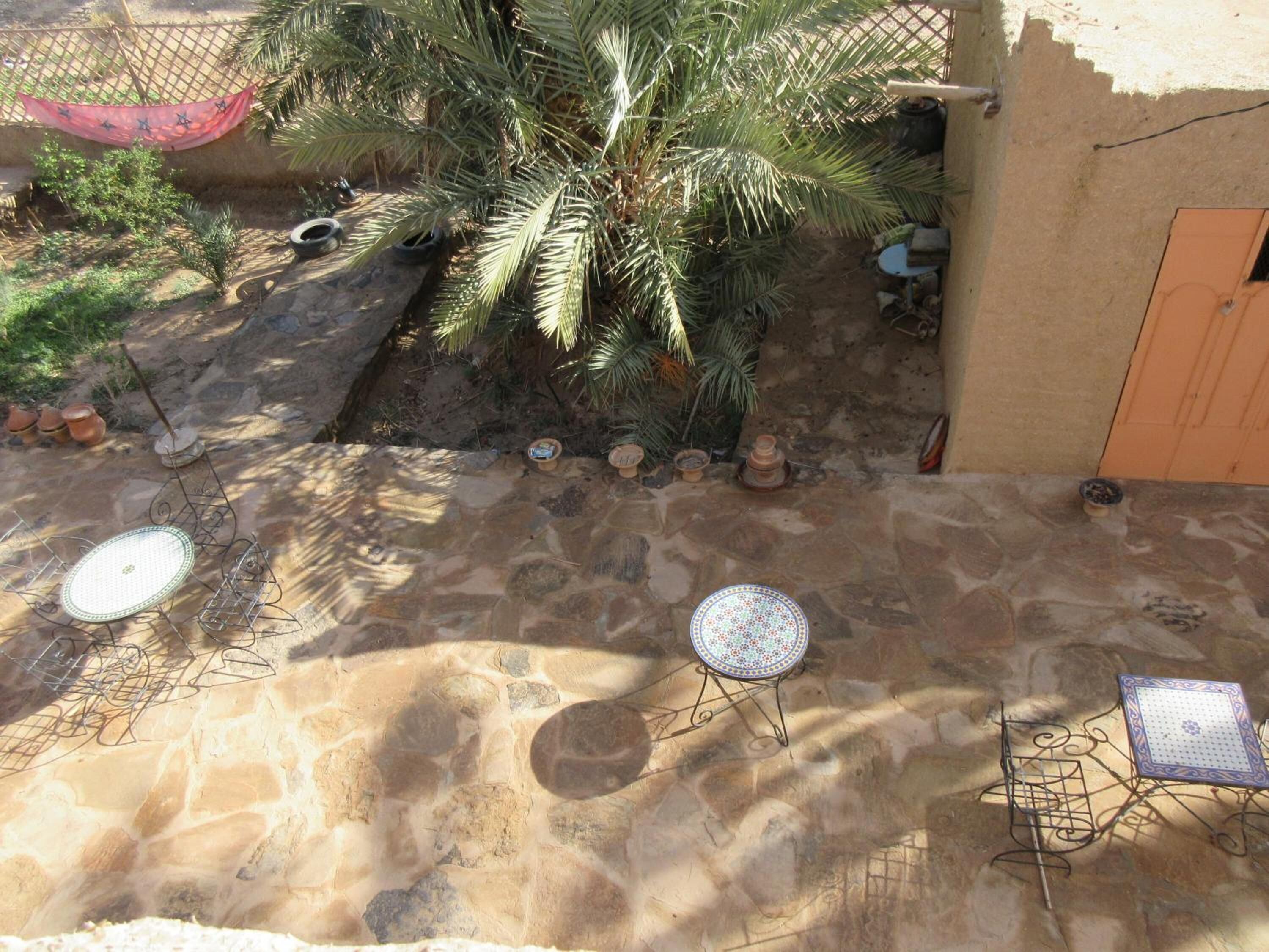 A courtyard with stone flooring, two metal tables, a palm tree, and a small garden area with pots.