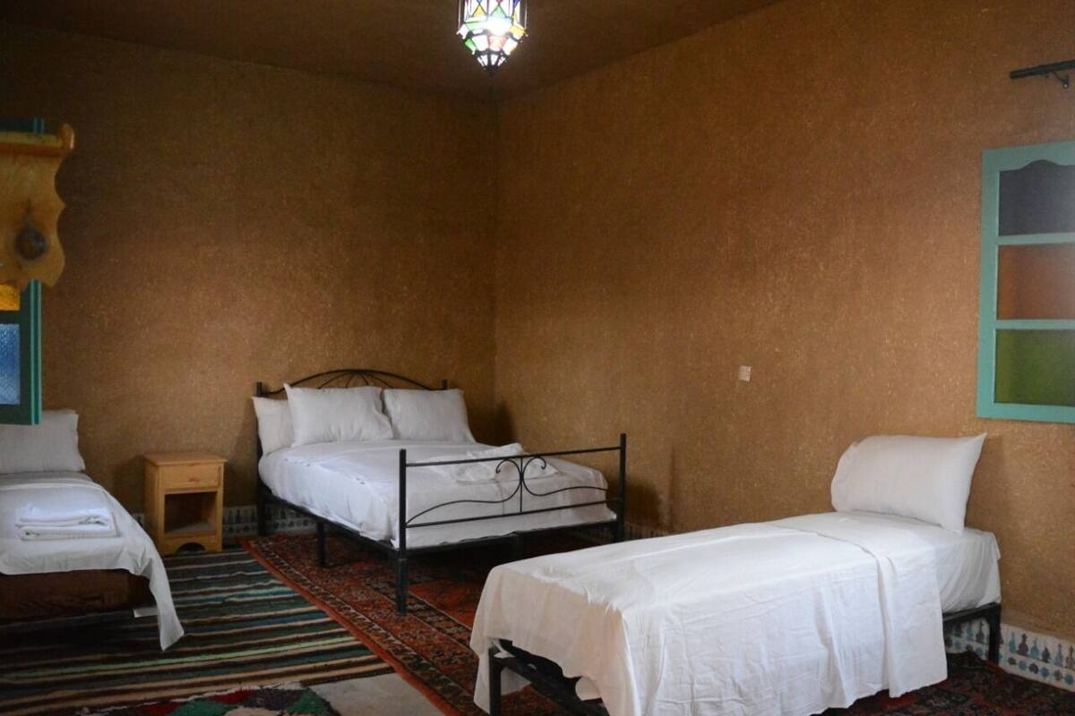 Une chambre avec deux lits, une petite table de chevet en bois, un tapis coloré et un lustre en vitrail.