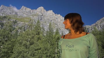 A person standing in front of a mountainous landscape with trees and rocky cliffs.
