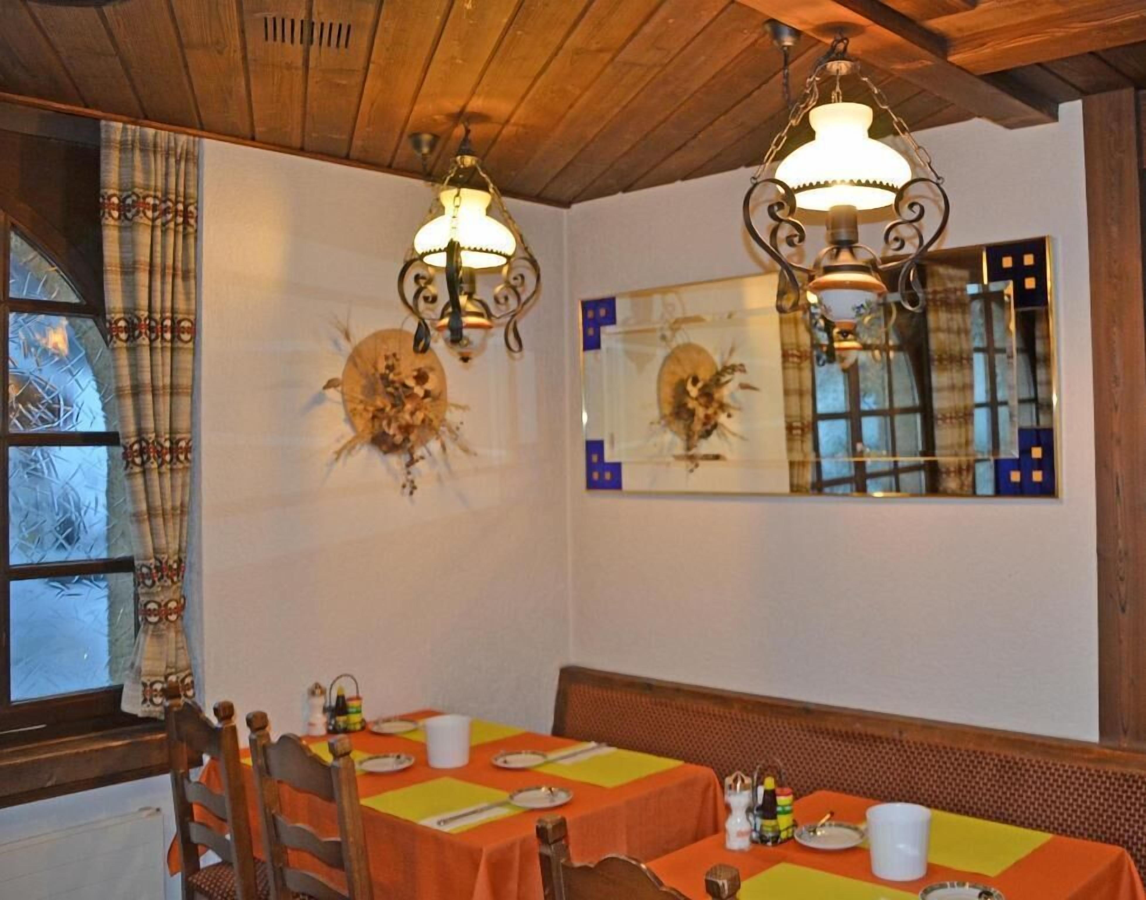 A dining area with wooden ceiling beams, two wall-mounted chandeliers, a large mirror, and a table set with plates and cutlery.