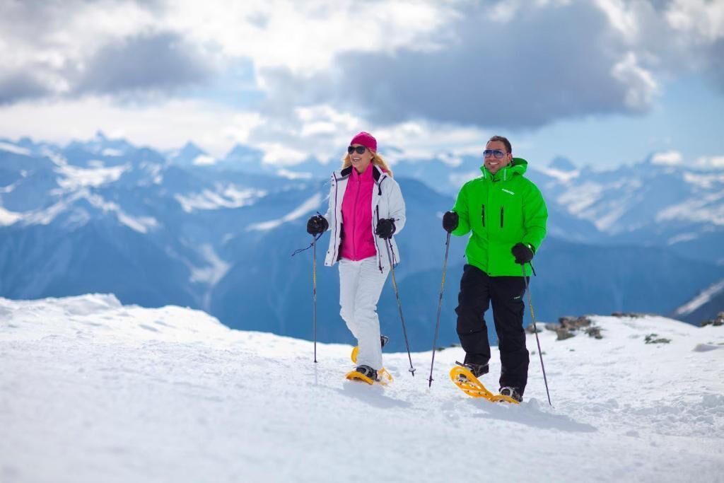 Dos personas esquiando en una montaña nevada con cielo despejado y montañas distantes al fondo.