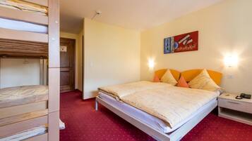 Una habitación de hotel con literas, una cama individual con almohadas naranjas, una mesita de noche con un teléfono y un cuadro en la pared.