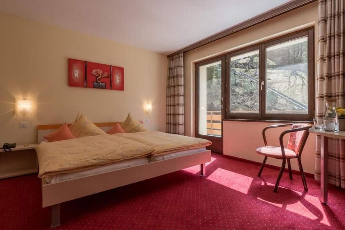 Un dormitorio con cama, una silla, un escritorio y una ventana con vista a árboles.