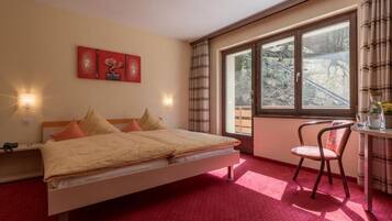 A bedroom with a bed, a chair, a desk, and a window with a view of trees.