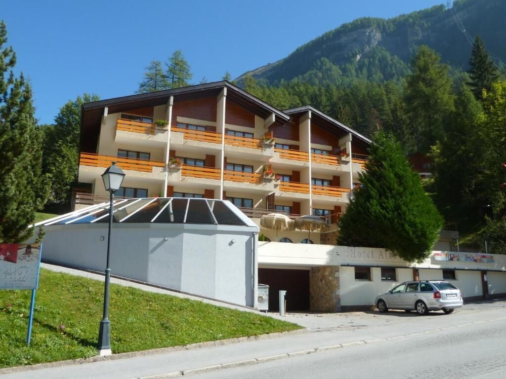 Ein mehrstöckiges Hotel mit Balkonen, einem Parkplatz und einer Bergkulisse.