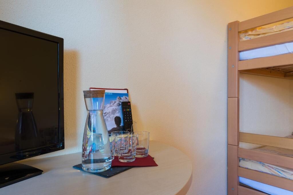 A room with a TV, a water bottle, glasses, and a bunk bed.