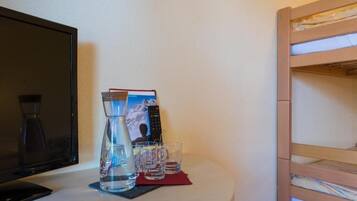 A room with a TV, a water bottle, glasses, and a bunk bed.