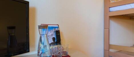 Una habitación con televisión, una botella de agua, vasos y una cama litera.