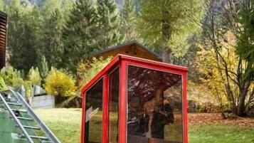 A red Alex Express tram station with a glass enclosure, set against a backdrop of trees and a mountain.