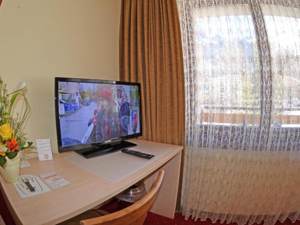 Een hotelkamer met een televisie op een bureau, een vaas met bloemen en een raam met gordijnen.