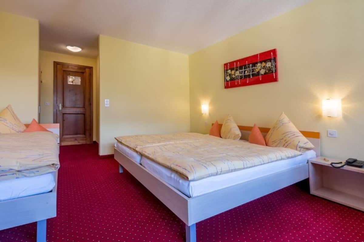 Habitación de hotel con dos camas, alfombra roja, puerta de madera y una obra de arte roja en la pared.