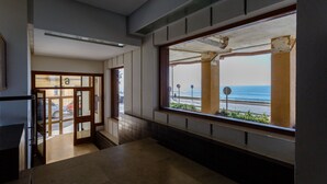 A hallway with a large window overlooking the sea, a tiled floor, and a door leading to another room.