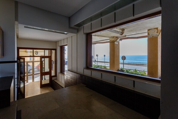 A hallway with a large window overlooking the sea, a tiled floor, and a door leading to another room.